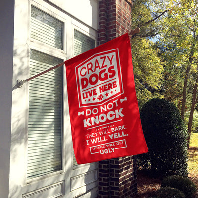 red house flag hung up on wall with text "crazy dogs live here do not knock they will bark, i will yell, things will get ugly"